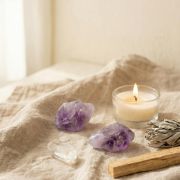 Amethyst Rohstein in violett auf einem natürlichen Stoff, umgeben von Kerze und Räucherstäbchen.