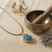 Nahaufnahme des blauen Apatit Anhängers mit goldener Fassung auf hellem Hintergrund.