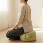 Frau sitzt auf gelbem Bio Meditationskissen für Yoga und Meditation.