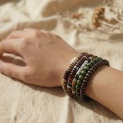 Hand mit Holz Armband Set in Braun, Grün und Creme auf neutralem Hintergrund.