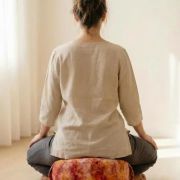 Frau sitzt meditierend mit geschlossenen Augen auf dem runden Chakra Meditationskissen – warme Farbtöne in Rot und Bordeaux unterstützen Erdung und Ruhe, pflanzengefärbter Baumwollbezug, gefüllt mit Bio Dinkelspelz für aufrechte Haltung, achtsame Szene für Yoga, Zazen, oder spirituelle Praxis, veganes, nachhaltiges Sitzkissen als kraftvoller Begleiter für Körperbewusstsein und Selbstverbindung.