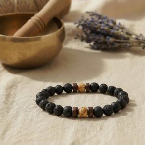 Nahaufnahme eines schwarzen Lava-Armbands mit zwei braun-marmorierten Bildstein-Perlen auf Stein-Untergrund.