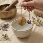 Goldenes Tee-Ei und roher Amethyst-Edelstein liegen auf hellem Leinen neben einer Klangschale.