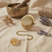 Sonnenlicht bricht sich in den Facetten des rohen Citrin-Steins, der an der goldenen Kette über einer rustikalen Holzoberfläche hängt.