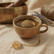 Goldenes Teesieb und roher Citrin-Edelstein liegen auf hellem Leinen neben getrockneten Orangenscheiben.