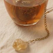 Arrangement aus dem Citrin-Tee-Ei, gelben Blumen und einer Kerze für ein sonniges Wellness-Gefühl.