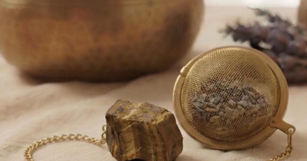 Goldenes Tee-Ei und roher Amethyst-Edelstein liegen auf hellem Leinen neben einer Klangschale.
