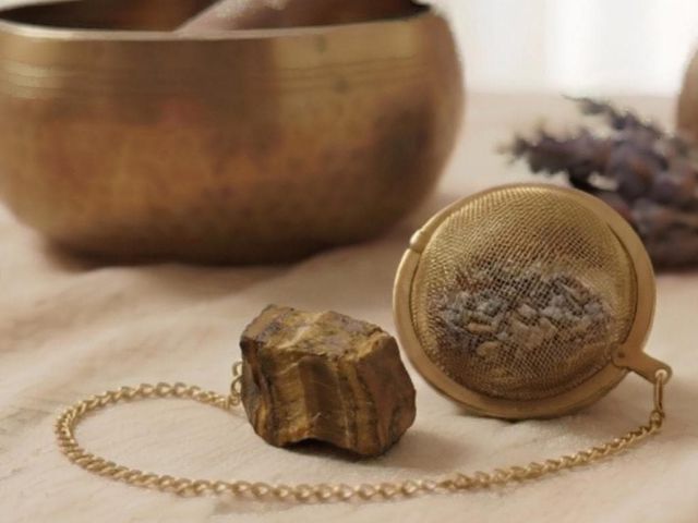 Goldenes Tee-Ei und roher Amethyst-Edelstein liegen auf hellem Leinen neben einer Klangschale.