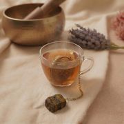 Arrangement aus goldenem Teesieb, Abtropfschale, Amethyst, getrocknetem Lavendel und einer tibetischen Klangschale im Hintergrund.