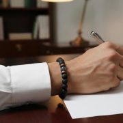 Detailaufnahme eines schwarzen Lavastein-Armbands an einer Hand beim Schreiben.