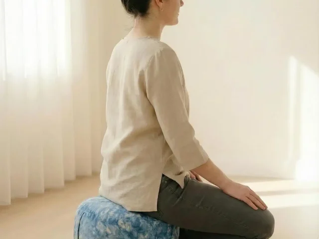 Seitliche Ansicht einer Frau beim Meditieren auf dem Vishuddha Chakra-Kissen – ergonomischer Sitz, entlastet Rücken und Nacken sanft.