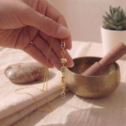 Chakra Halskette in Gold mit 7 bunten Steinen, von Hand gehalten.