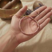 Rhodonit Armband in Hand gehalten, zarte rosa Perlen und goldene Akzente.